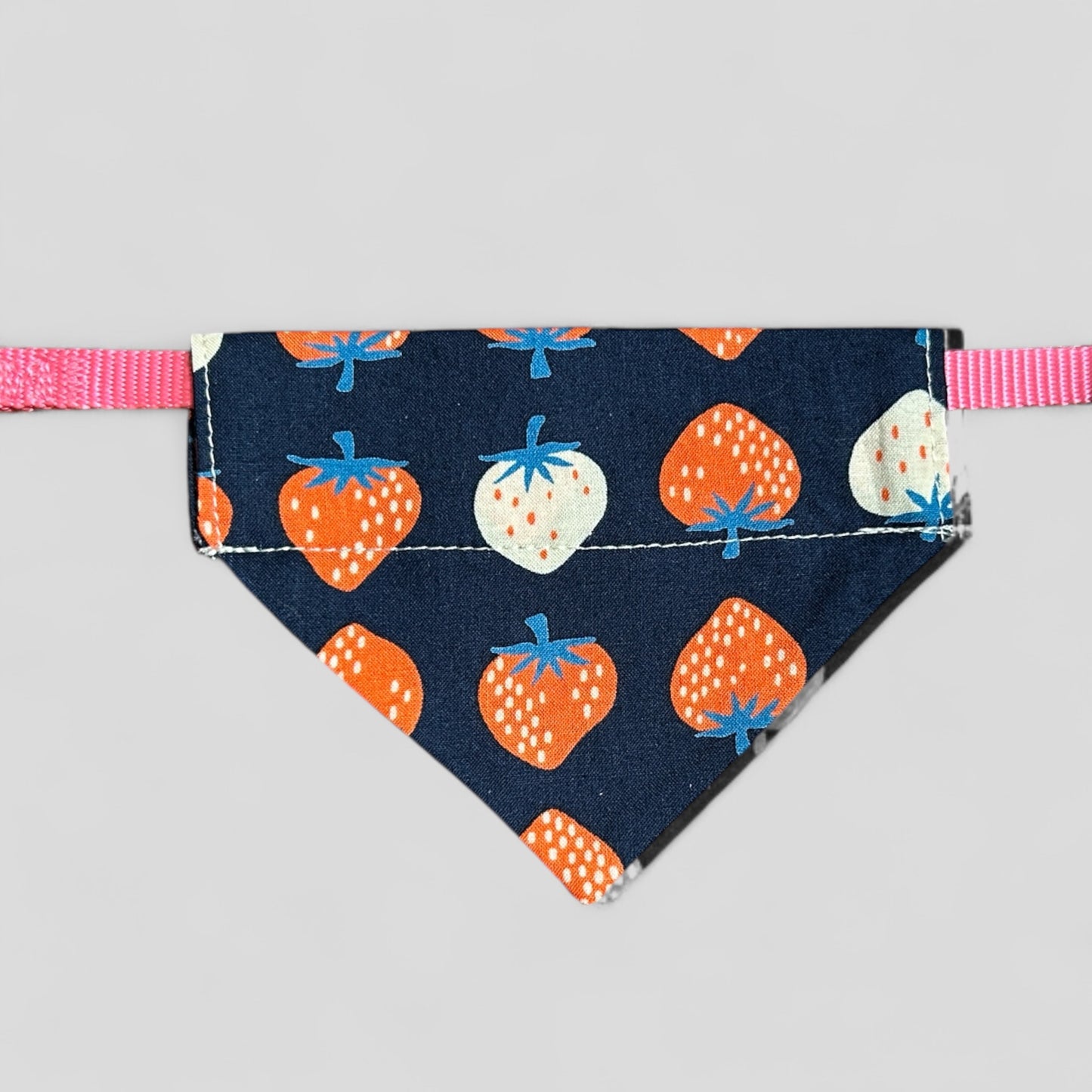 Dog bandana with strawberry pattern on a pink strap against a gray background