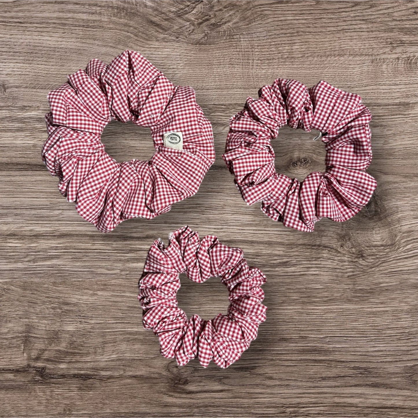 Three red and white checkered scrunchies on a wooden surface
