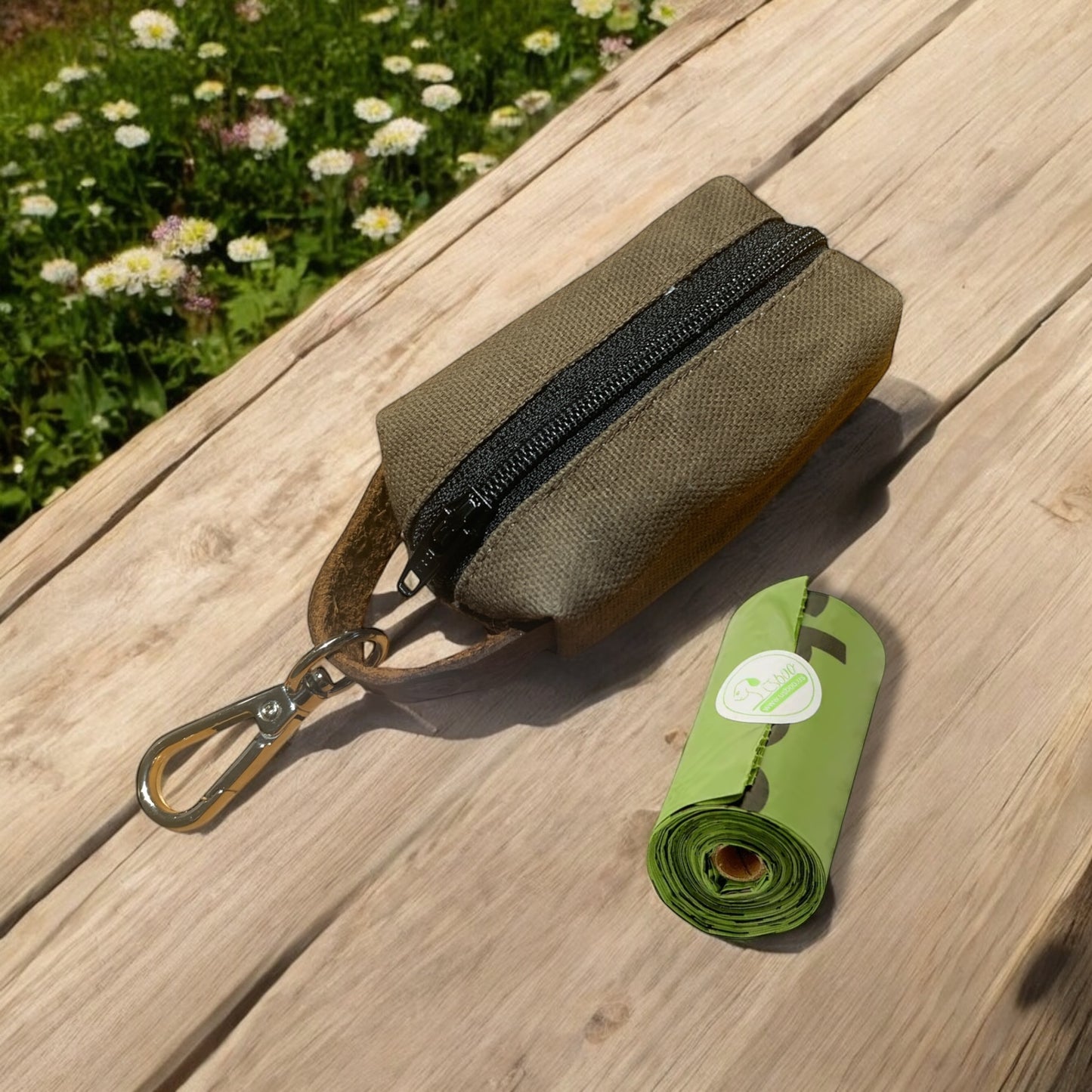 small waxed canvas dog poop bag holder with a muted brown exterior and a blue zipper, featuring a metal keychain clip and a yellow fabric loop for easy attachment. The durable, water-resistant design is ideal for carrying waste bags during dog walks. (brown on wood)