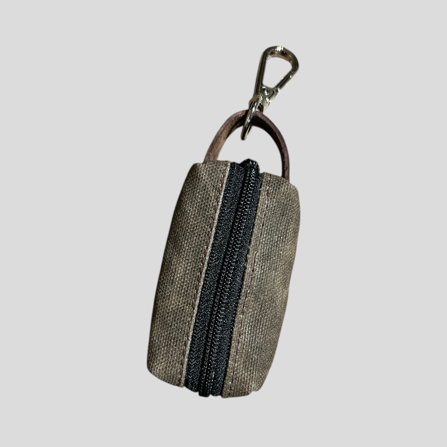 small waxed canvas dog poop bag holder with a muted brown exterior and a blue zipper, featuring a metal keychain clip and a yellow fabric loop for easy attachment. The durable, water-resistant design is ideal for carrying waste bags during dog walks. (brown)