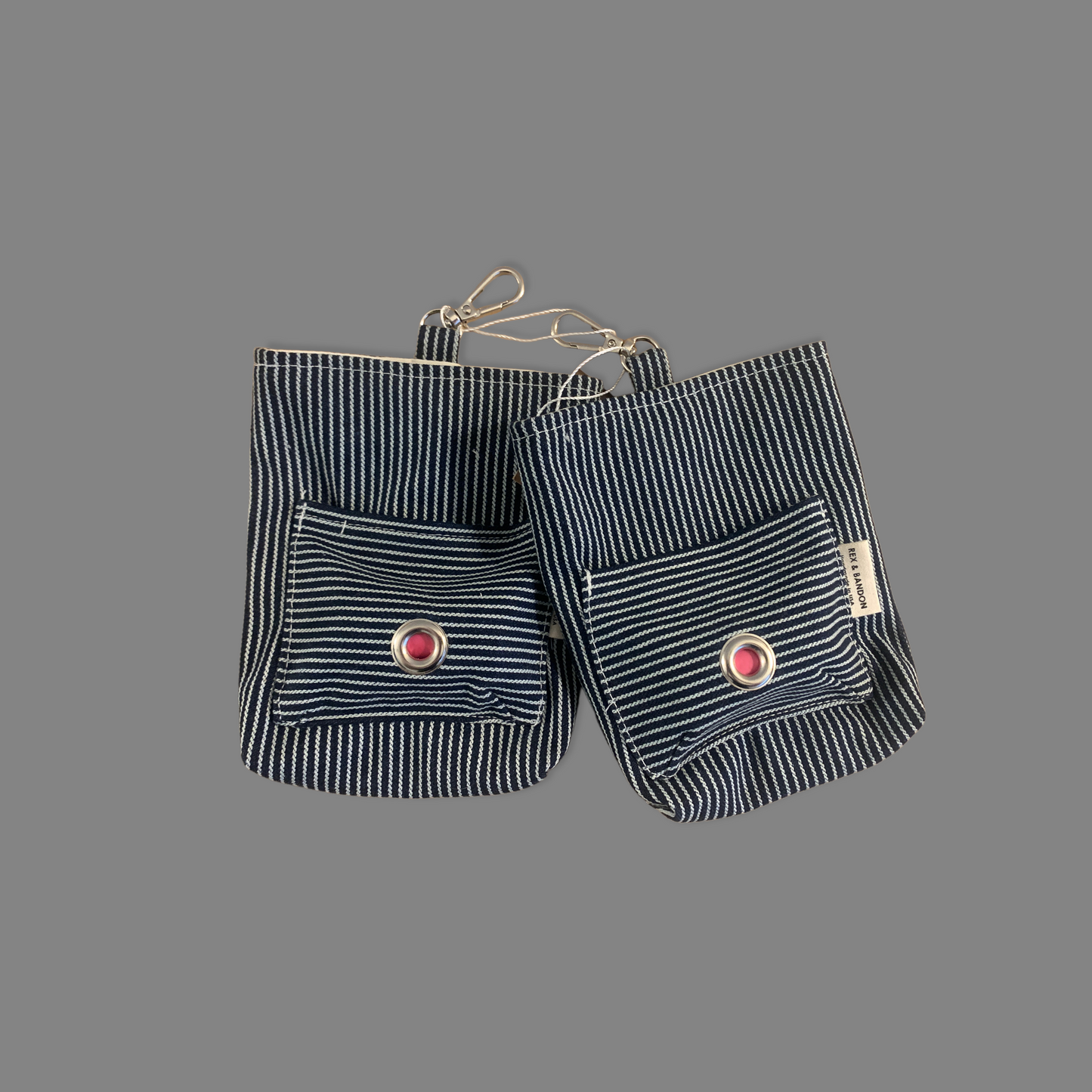 A striped cotton dog walker pouch with a front pocket and a carabiner clip, against a gray background.