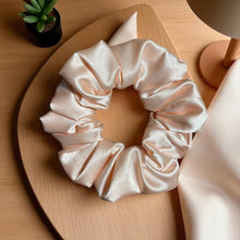 Load image into Gallery viewer, pink satin scrunchie on a wooden surface with a plant and lamp in the background