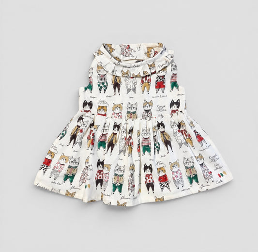 A sleeveless white pet dress featuring a playful print of various cartoon cats in colorful outfits, displayed flat against a neutral light gray background.