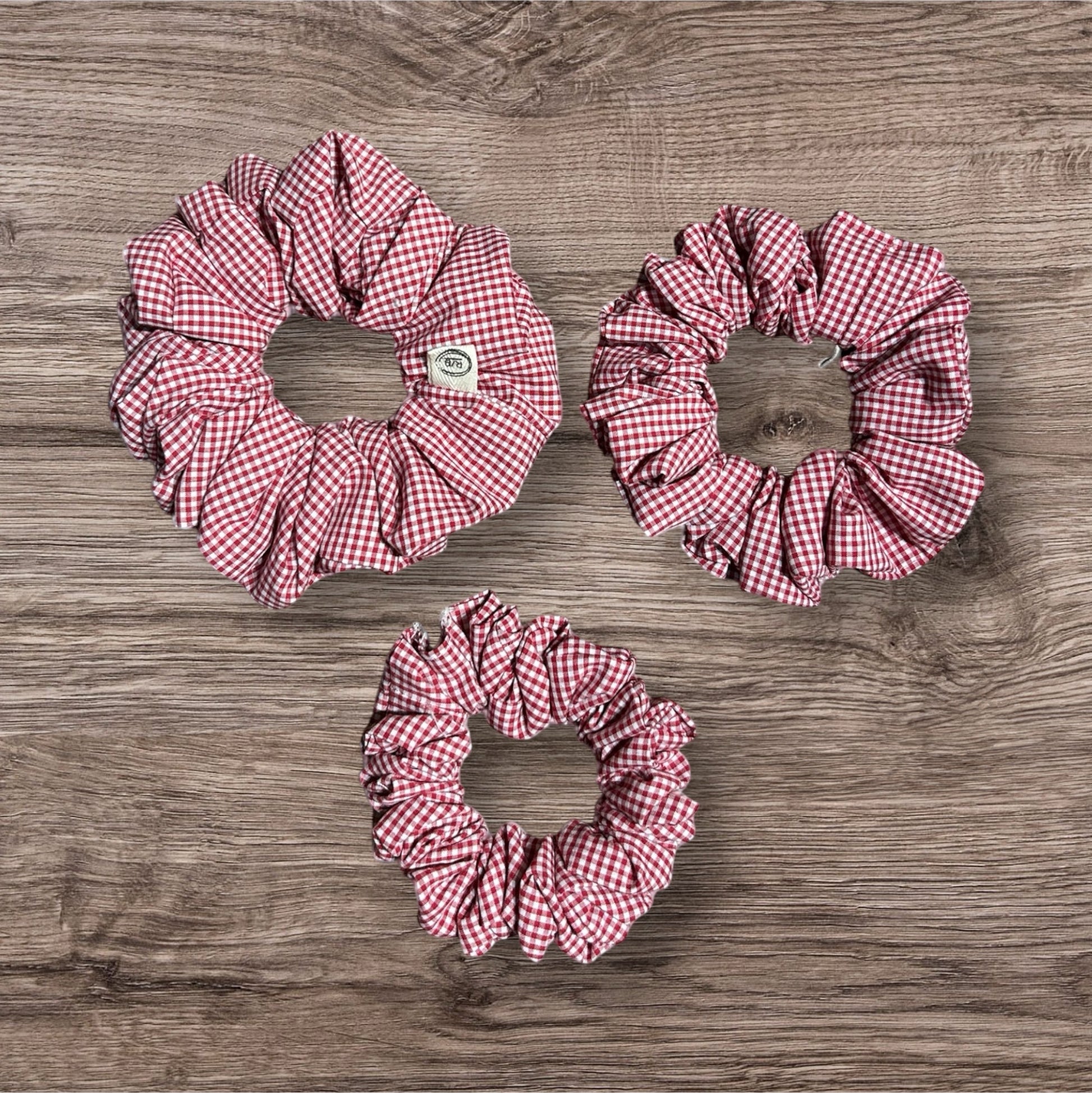 Three red and white checkered scrunchies on a wooden surface
