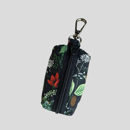 A floral print dog poop bag holder with a metal clip on the top, featuring a mix of roses and peonies in pink, green, and white colors.