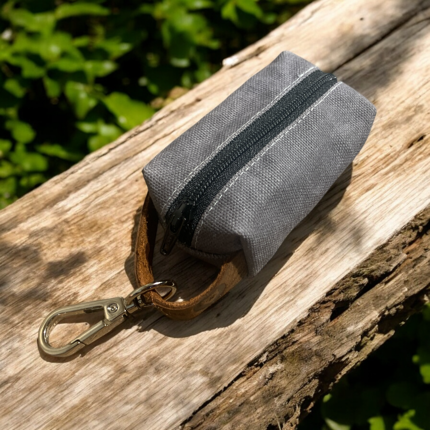 A gray waxed canvas dog poop bag holder with a sturdy metal clip and a black zipper.