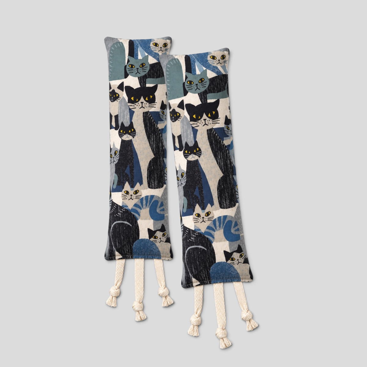 Two fabric cat toys with a pattern of black, blue, and white cats, featuring cream-colored rope tassel ends, displayed against a solid light gray background.