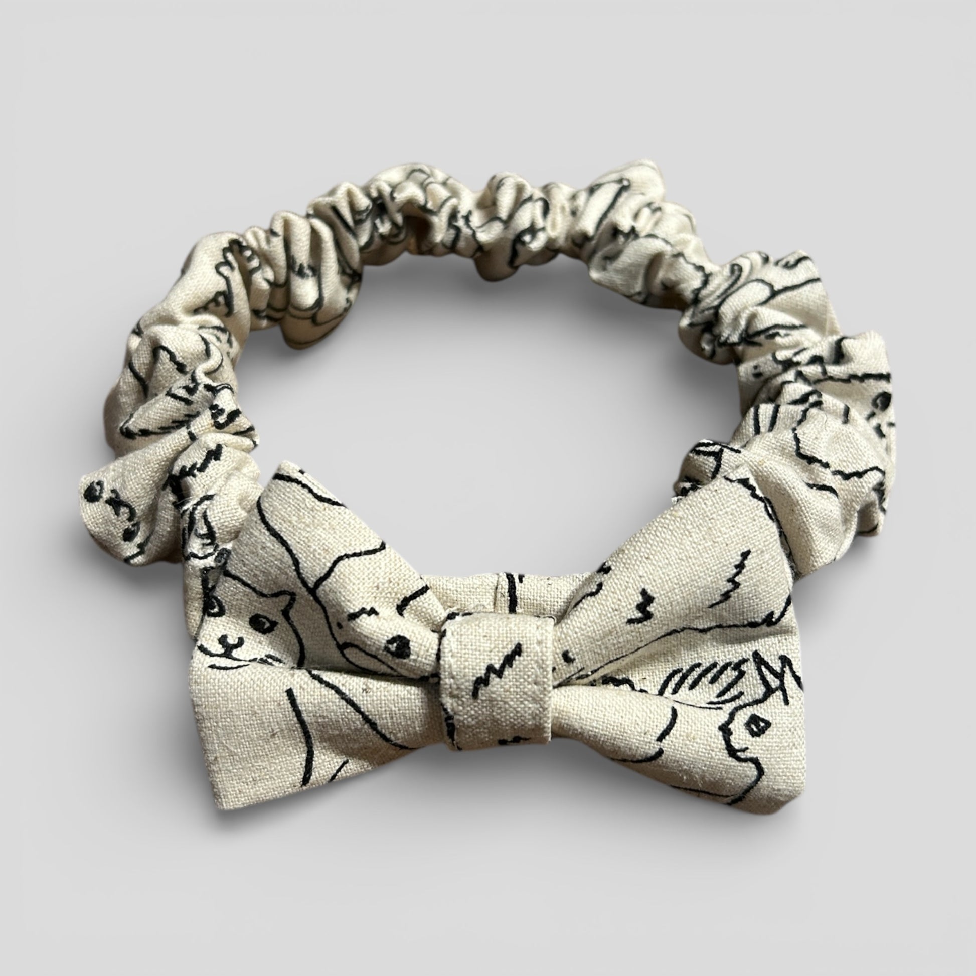 Beige bow tie with black cat illustrations on a light gray background