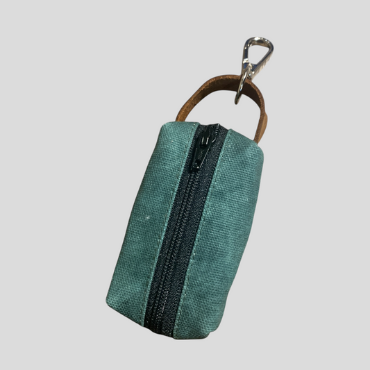 small waxed canvas dog poop bag holder with a muted brown exterior and a blue zipper, featuring a metal keychain clip and a yellow fabric loop for easy attachment. The durable, water-resistant design is ideal for carrying waste bags during dog walks. (hunter green, front view)