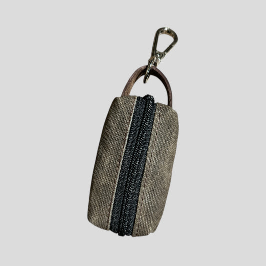 small waxed canvas dog poop bag holder with a muted brown exterior and a blue zipper, featuring a metal keychain clip and a yellow fabric loop for easy attachment. The durable, water-resistant design is ideal for carrying waste bags during dog walks. (brown)