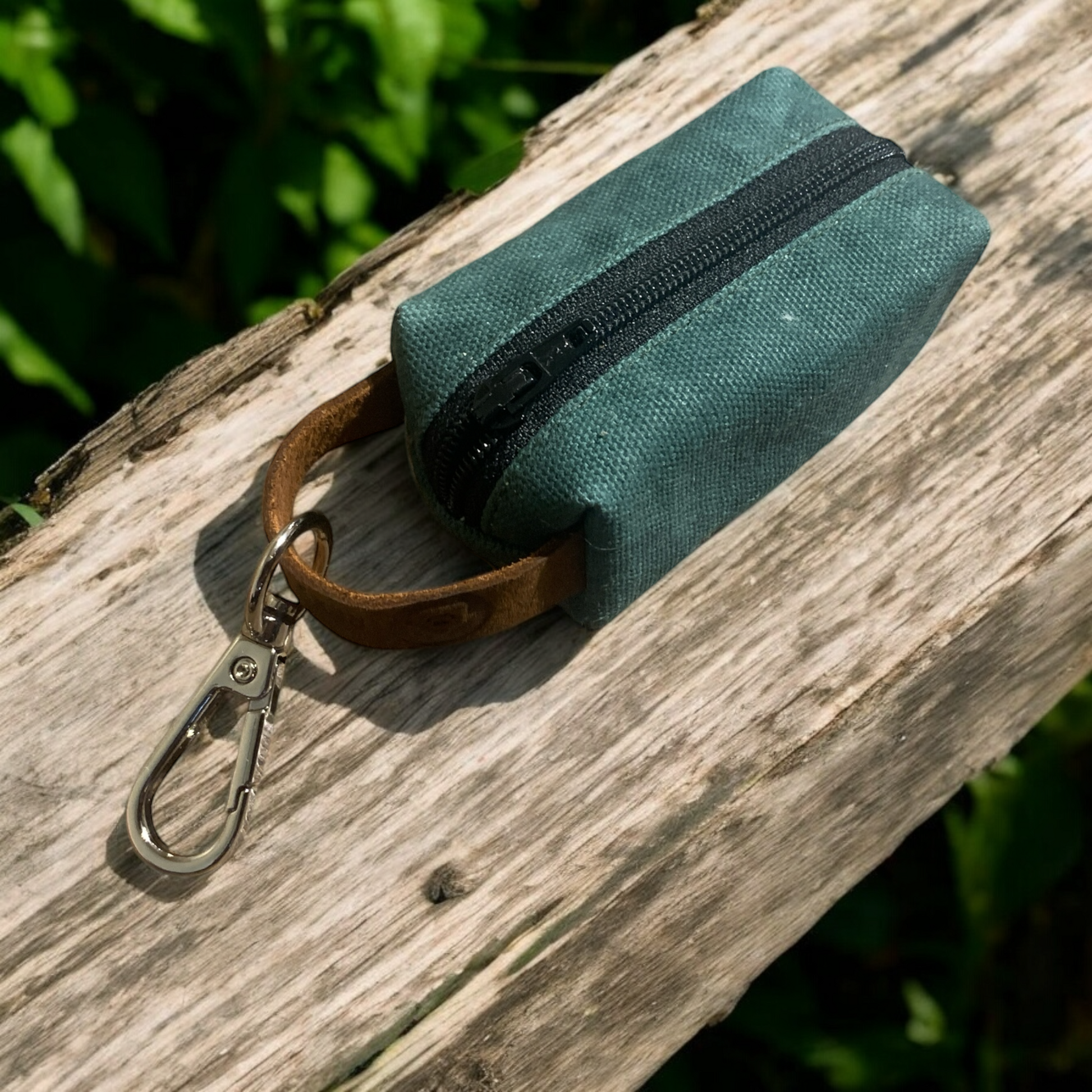 small waxed canvas dog poop bag holder with a muted brown exterior and a blue zipper, featuring a metal keychain clip and a yellow fabric loop for easy attachment. The durable, water-resistant design is ideal for carrying waste bags during dog walks. (hunter green
