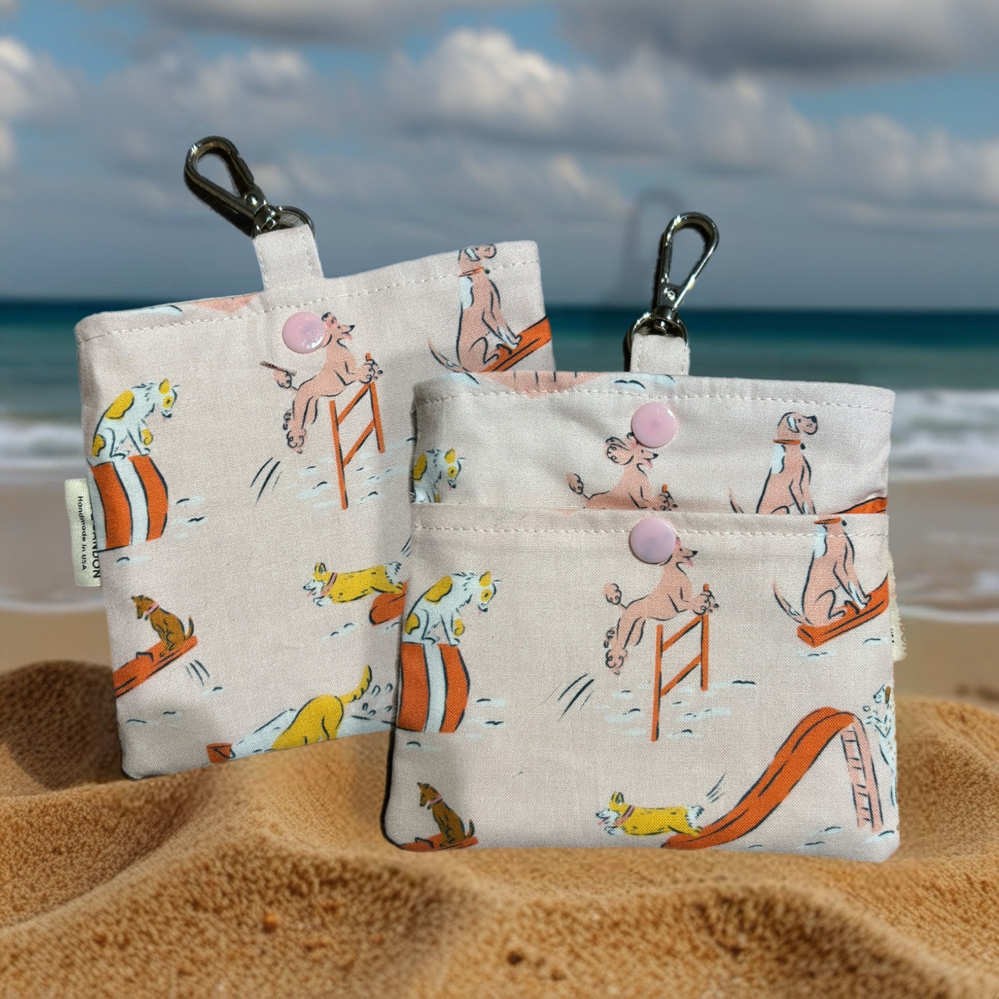 Two small pouches with beach-themed designs on a sandy surface with ocean in the background