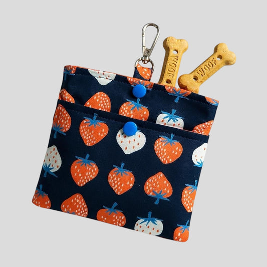 Fabric pouch with strawberry pattern containing dog toys on a light gray background