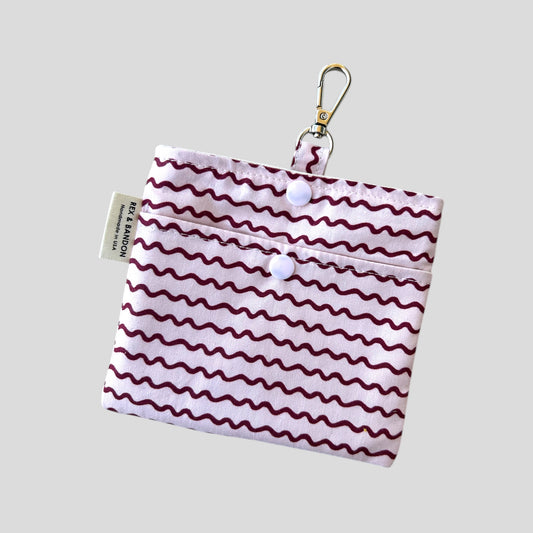 A small fabric pouch with a floral design featuring pink, red, and yellow roses, green leaves, and red berries on a light green background. The pouch has a snap closure, a metal keychain clip attached to a fabric loop, and a "Handmade in USA" label.