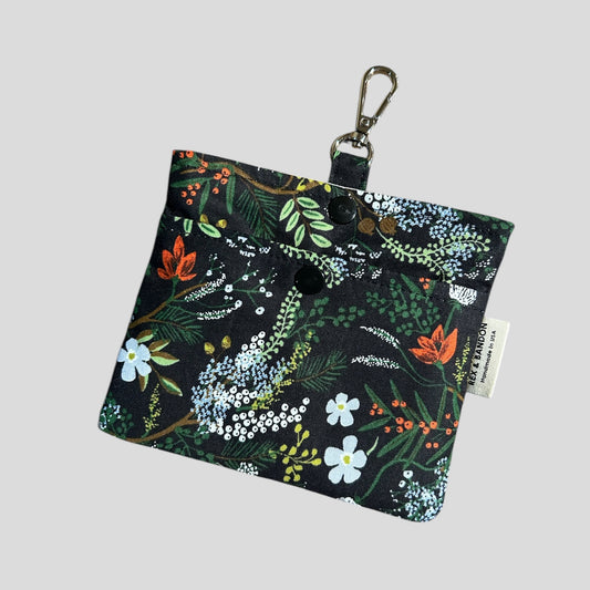 A small fabric pouch with a floral design featuring  English Rose | Juniper Forest | on a black background. The pouch has a snap closure, a metal keychain clip attached to a fabric loop, and a "Handmade in USA" label.
