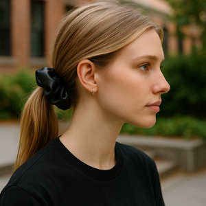 Woman with a black scrunchie in her hair, wearing a black shirt, outdoors.