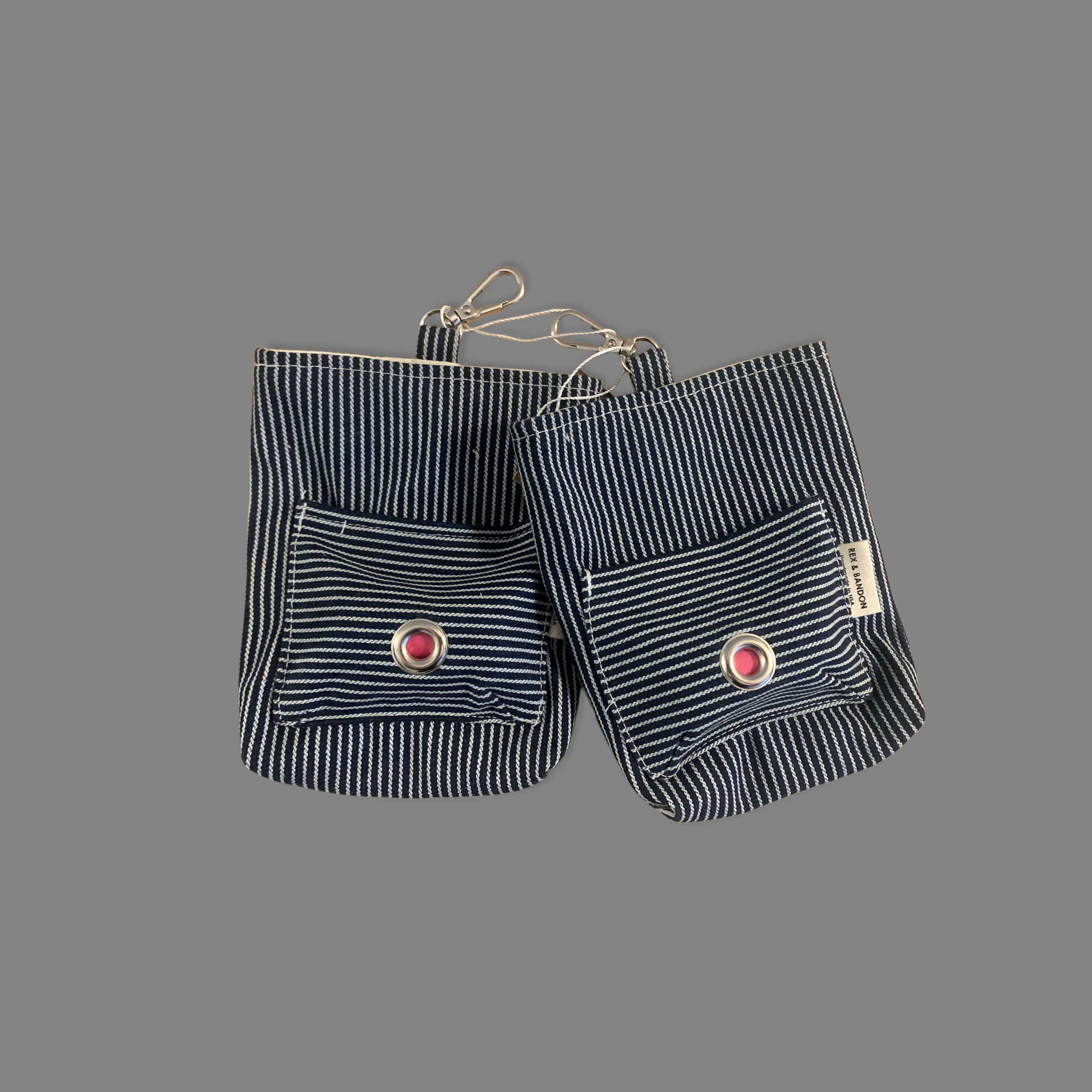 A striped cotton dog walker pouch with a front pocket and a carabiner clip, against a gray background.